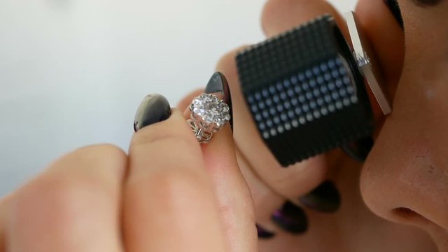 Woman looking at the earring with diamonds through jeweler's loupe. Jeweler evaluates the value of the luxury earrings with jems