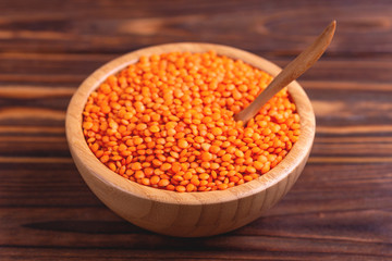 Raw red lentils in wooden bowl on rustic wooden background