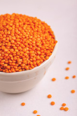 Raw red lentils in clay bowl on white marble background