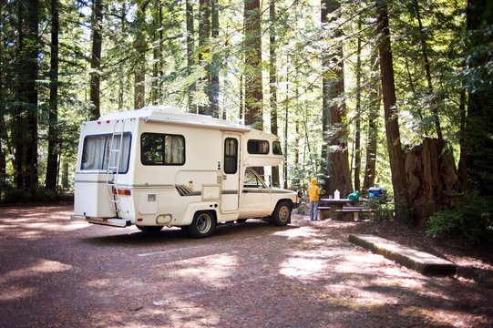 Rear view of boy standing by camper van in forest