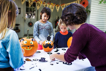 Naklejka premium Mother assisting children in decorating pumpkins at table during Halloween party