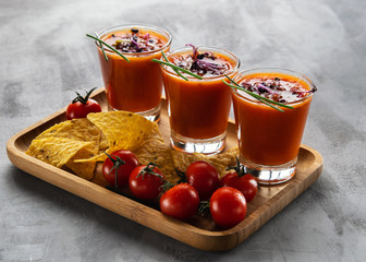 Tomato soup gazpacho in glasses with sprouted sprouts accompanied with corn chips on light gray background.
