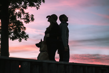 silhouettes of a couple with dog standing back on back at sunset