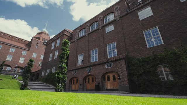 Beautiful architecture and brick construction of large buildings that house offices and classrooms on a university campus. Heavey wooden doors. Green grass and bright blue sky. DOLLY BACK and RIGHT.