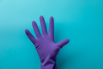 A gloved hand shows five fingers on a blue background. Blue latex glove on the hand of a doctor or...