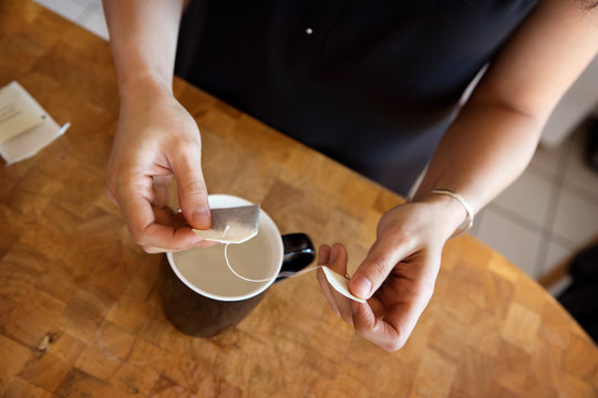Midsection of woman holding teabag over mug at kitchen counter
