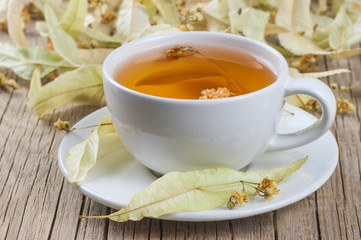 white cup linden tea or blooming tilia, basswood, on rustic vintage wooden table. Herbal tea concept, selective focus
