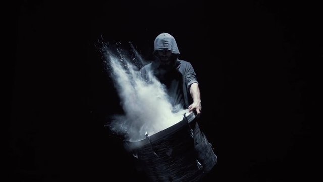 hooded man beats drum with flour