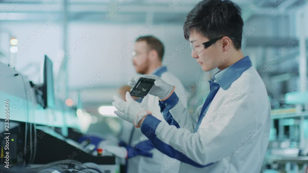 Poster high-tech factory: quality control engineer picks up and visually checks smart electronic device for