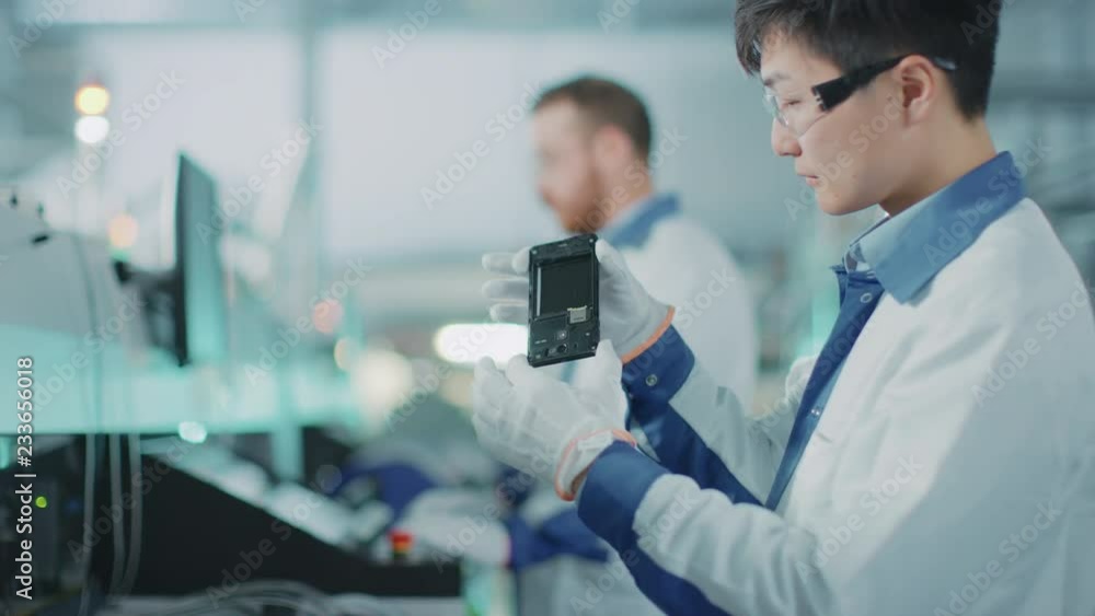 Poster high-tech factory: quality control engineer picks up and visually checks smart electronic device for