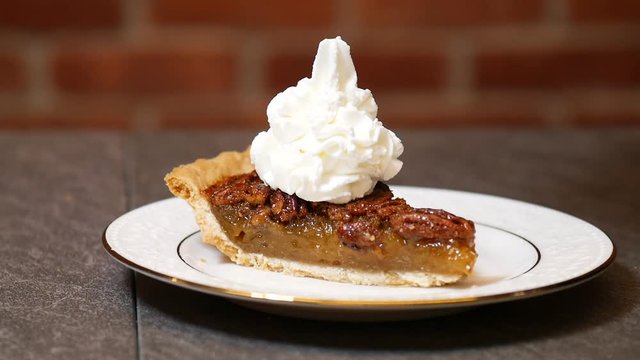Close up, person pours whipped cream on slice of pecan pie