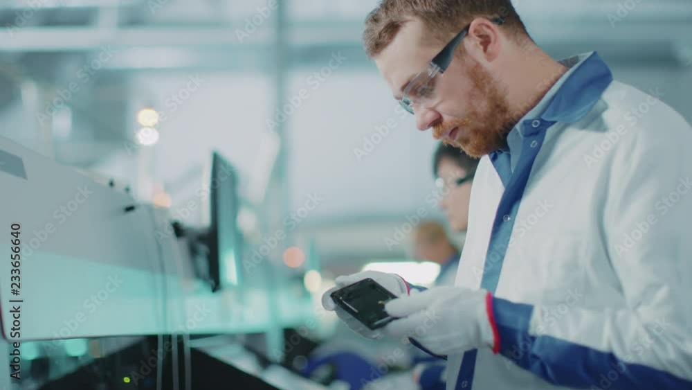Poster high-tech factory: quality control engineer picks up, visually checks smart electronic device for po