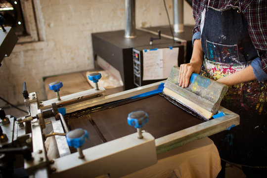 Midsection of woman pressing ink on frame in workshop