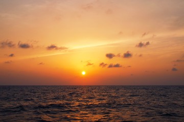 Golden sunset over sea horizon with clouds and light streak over sky during dusk and choppy waves