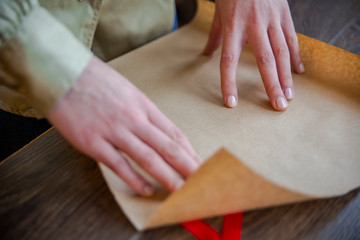 Obraz na płótnie Canvas Hands of beautiful young woman wrapping present in brown paper 