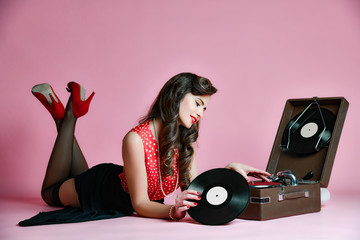 Glamorous pinup girl lying near retro gramophone holding LP vinyl record looking up on pink...