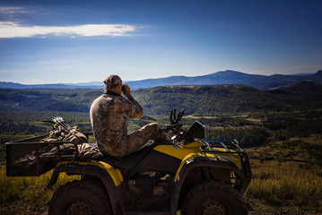 Hunter looking at mountains through binoculars while sitting on quadbike © Cavan for Adobe
