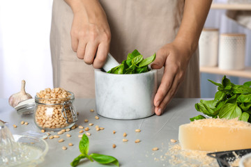 Woman making basil pesto sauce at kitchen table