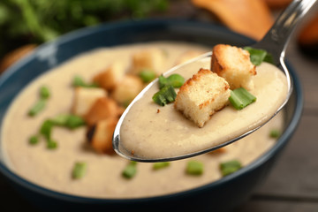 Spoon with fresh homemade mushroom soup over bowl, closeup