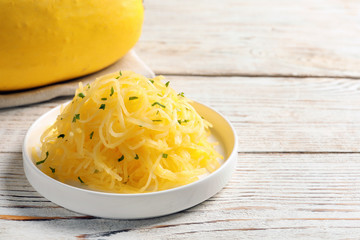 Plate with cooked spaghetti squash on wooden table. Space for text