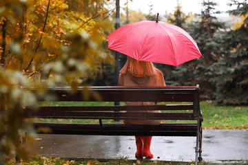 Woman with umbrella sitting on bench in autumn park. Rainy day