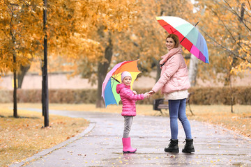 Mother and daughter with umbrellas taking walk in autumn park on rainy day