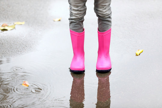 Little girl wearing rubber boots standing in puddle on rainy day, focus of legs. Autumn walk