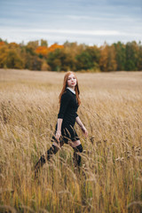 beautiful red-haired woman in a black dress walks on an autumn field.