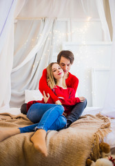 Fototapeta premium Fabulous couple in red sweaters posing on the bed
