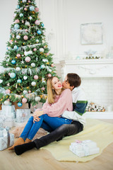 Sweet couple sitting near to a Christmas tree embracing each other