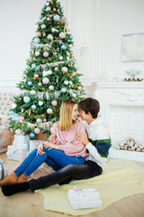 Magnificent couple sitting near to a Christmas tree embracing each other