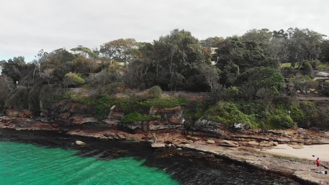 Drone lowering over water with men rock fishing in crystal clear water