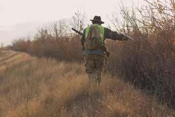 A hunter in a hat with a gun in camouflage and a reflective vest in the steppe