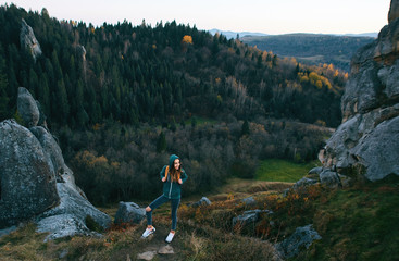 smiling woman hiker with backpack standing on edge of cliff against a forest background