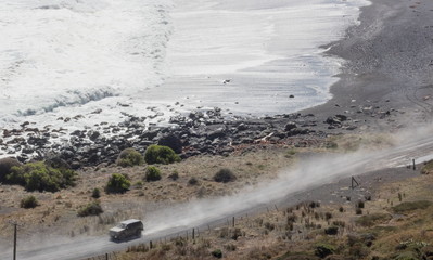 A 4wd vehicle driving on a coastal gravel road at Cape Palliser, New Zealand.