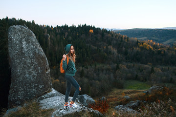 smiling woman hiker with backpack standing on edge of cliff against a forest background
