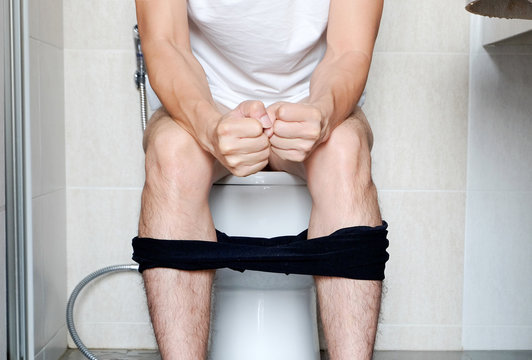 Man sitting in the toilet bowl. In the bathroom, his home is unhappy with constipation, diarrhea, food poisoning, health and medical concepts.