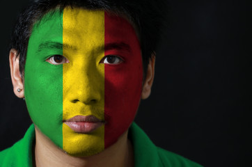 Portrait of a man with the flag of the Mali painted on his face on black background, A vertical tricolor of green gold and red.