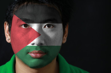 Portrait of a man with the flag of the Palestine painted on his face on black background, horizontal tricolor of black white and green; with a red triangle.