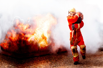 Brave Firefighter and holds saved boy in his arms in the midst of fire and smoke.in the background.