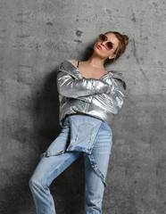 Sport woman in blue jeans in silver thin down puffer jacket standing on loft wall 