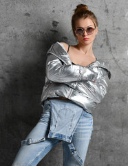 Sport woman in blue jeans in silver thin down puffer jacket standing on loft wall 