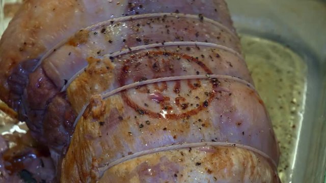 Stabbing a half cooked joint of pork in a glass roasting tray with a meat knife.