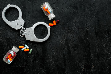 Arrest for illegal purchase, possession and sale drugs concept. Drugs as pills near handcuff on black background top view copy space