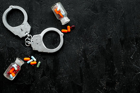 Arrest for illegal purchase, possession and sale drugs concept. Drugs as pills near handcuff on black background top view copy space