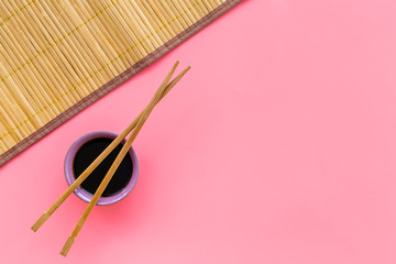 Chinese meal concept. soy sauce in bowl near chopsticks and bamboo table mat on pink background top...