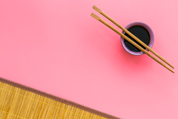 Fototapeta na wymiar Chinese meal concept. soy sauce in bowl near chopsticks and bamboo table mat on pink background top view space for text pattern