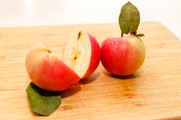 Cut half of the apple with leaf on cutting board on wooden table in soft-focus in the background, closeup. Delicious sweet and juicy fruits for salad cooking or bakery for background or wallpaper.