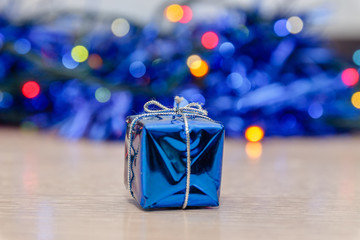 Merry christmas and happy new year greeting card. Close-up of christmas blue gift box against a tinsel and decorations background. Celebration Concept for New Year Eve in soft-focus in the background.