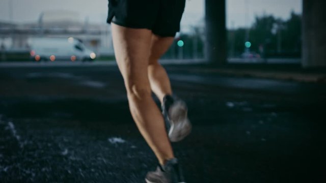 Legs Close Up of a Beautiful Strong Fitness Girl in Black Athletic Top and Shorts that Starts Sprinting. She is Running in an Urban Environment Under a Bridge with Cars in the Background.